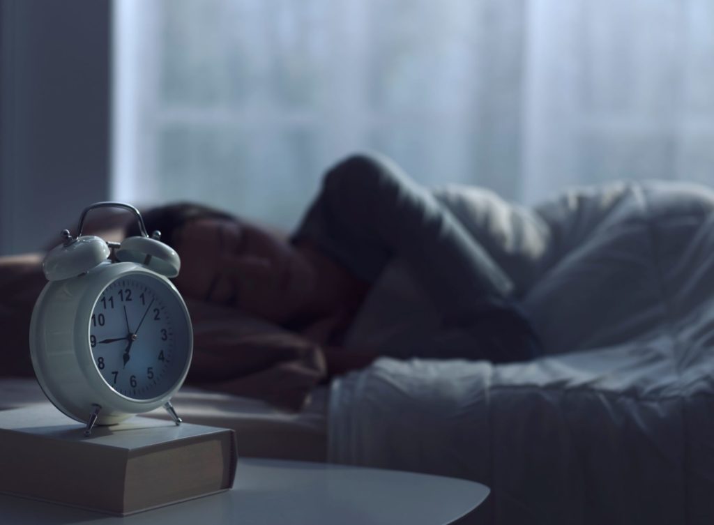 Someone asleep with alarm clock in focus