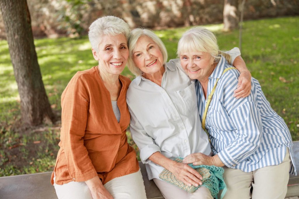 Three old women sitting on a bench in a park smiling 